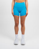 Front view of a woman wearing the Azure Blue Nexletica Synergy Rise Shorts, showing the high-rise waistband, 5-inch inseam and side pockets